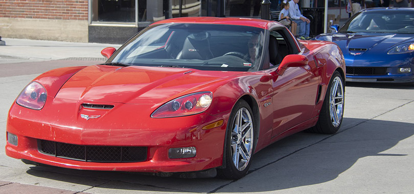 an old man driving a red Chevrolet Corvette