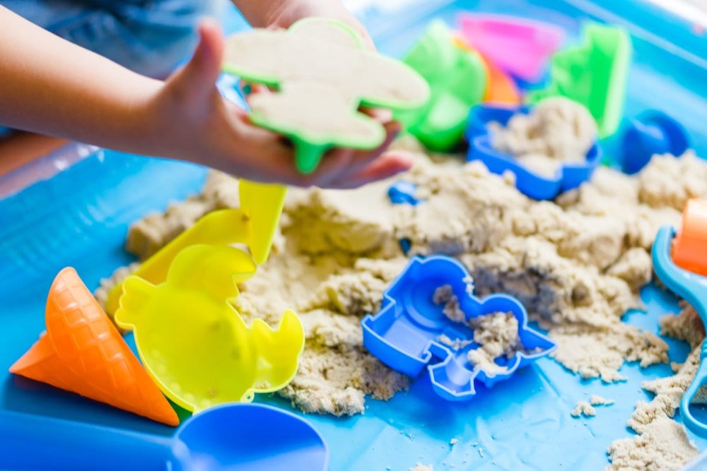 Child's hand holding shovel plastic toy with sand playing sand basket at home