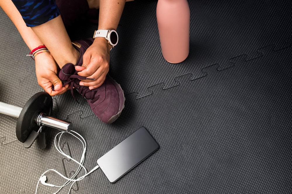 Woman tying shoes on black rubber tiles in home gym