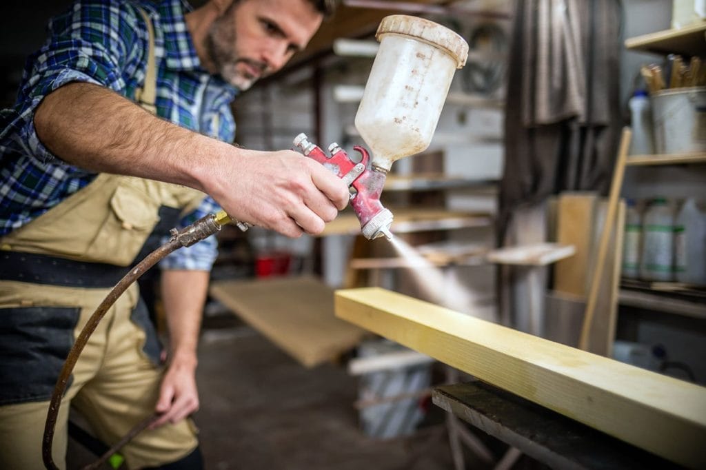 man paint spraying a wood plank