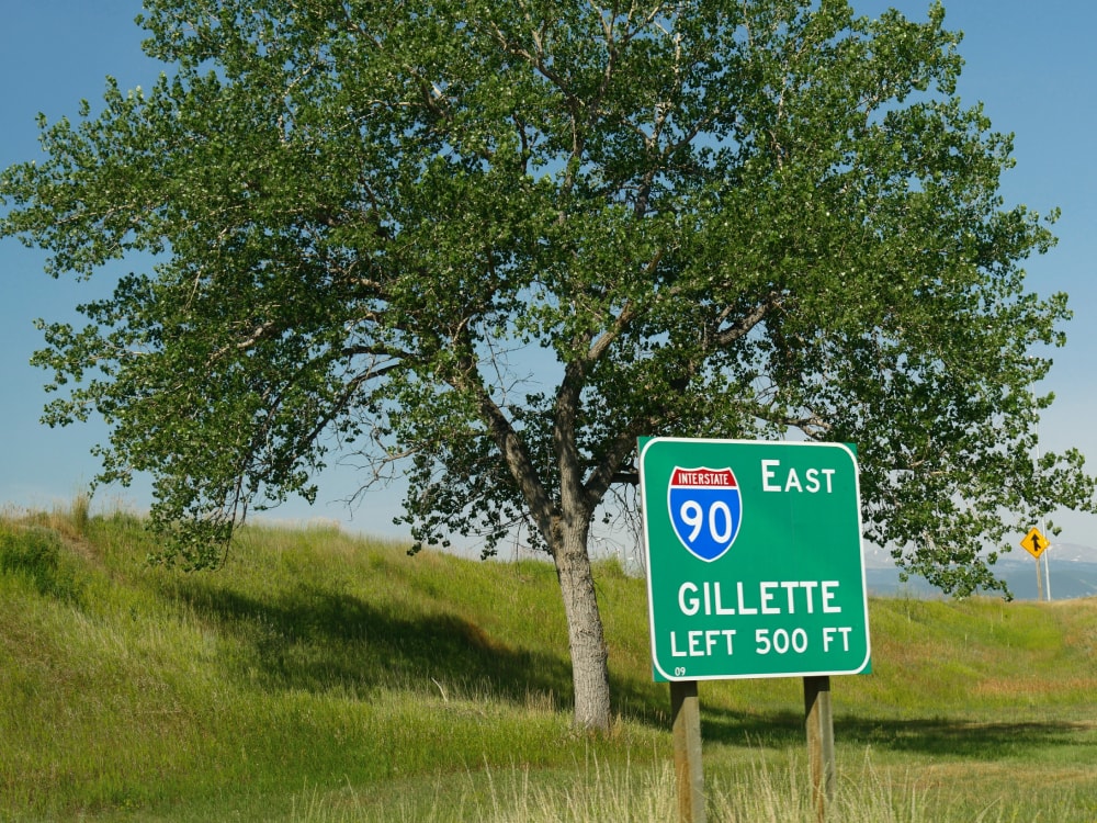 Roadside sign by a tree at Interstate 90 with distance to Gillette, Wyoming