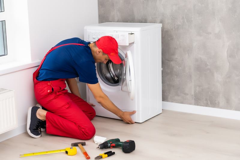 Plumber in overalls with tools is repairing a washing machine