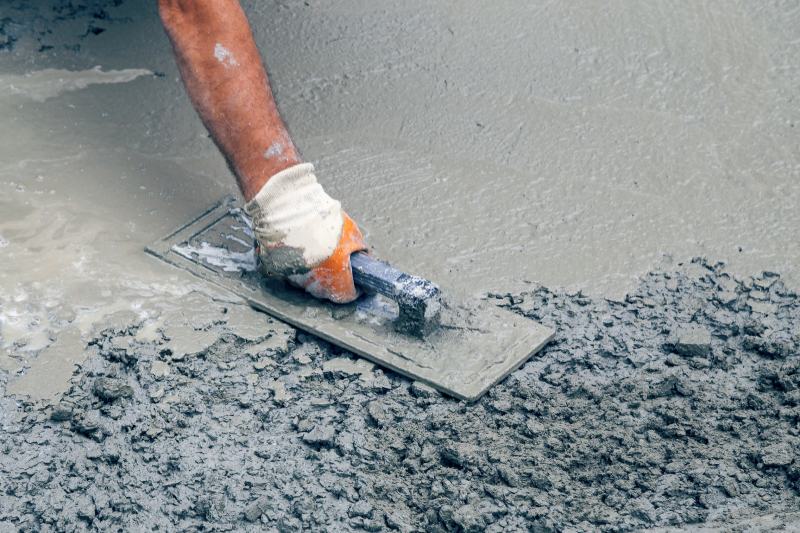 Hand builder with trowel leveling concrete slab and spreading poured