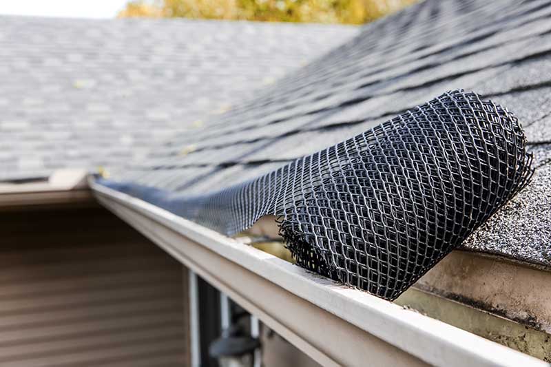 Roll of plastic mesh guard over gutter on a roof