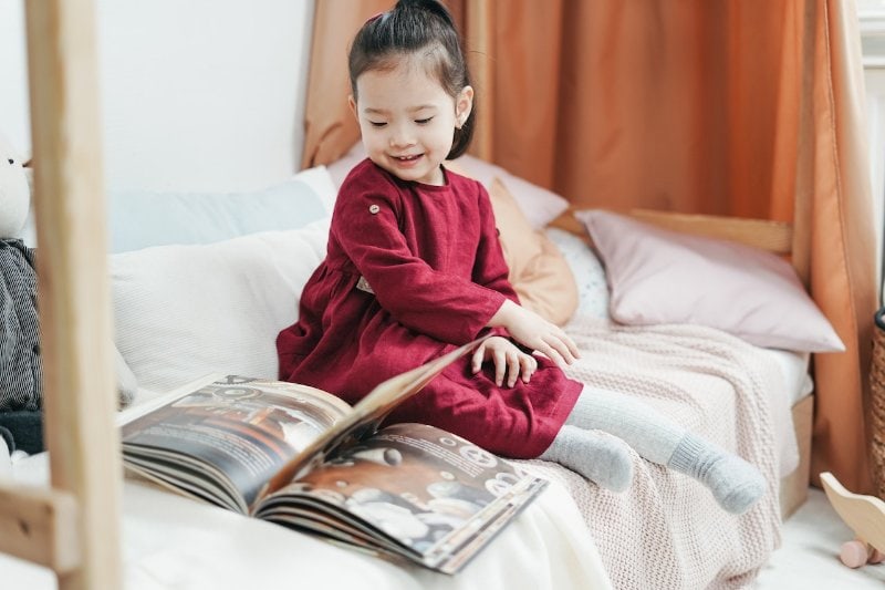 niña sentada en una cama pequeña leyendo