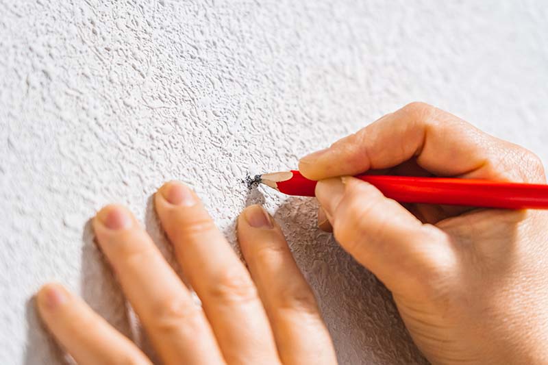 A woman marking the white wall with a red carpenter's pencil