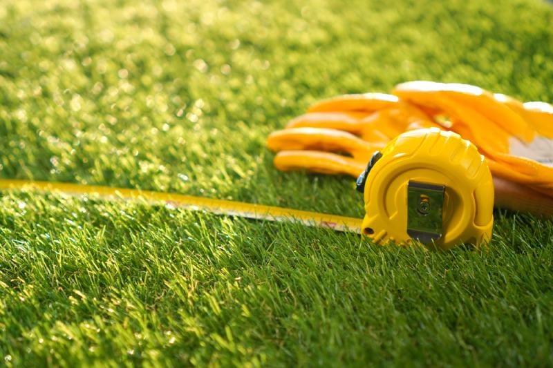 Artificial grass background with measuring tape and worker glooves