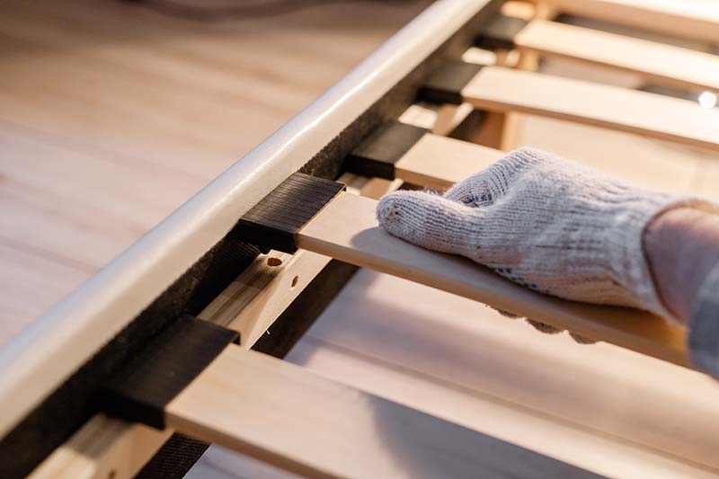 El trabajador masculino entrega el guante para armar la cama, conecta los listones al marco de la cama