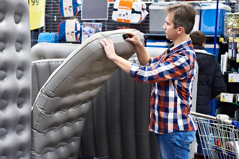 Man chooses an inflatable tourist sleeping pad for a hike in a sports shop