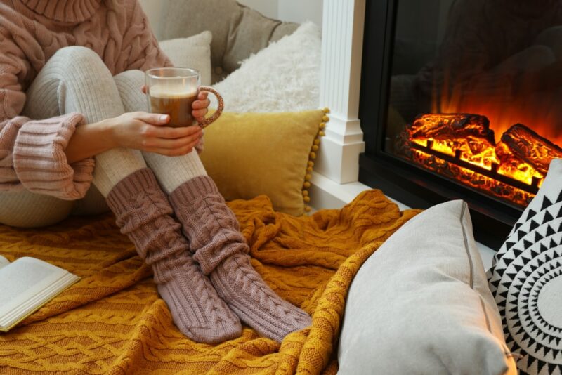 Woman with cup of coffee sitting near burning fireplace