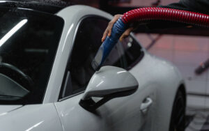 person holding a vacuum hose to clean a white car