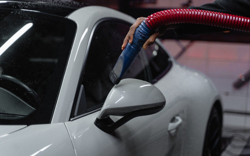 person holding a vacuum hose to clean a white car