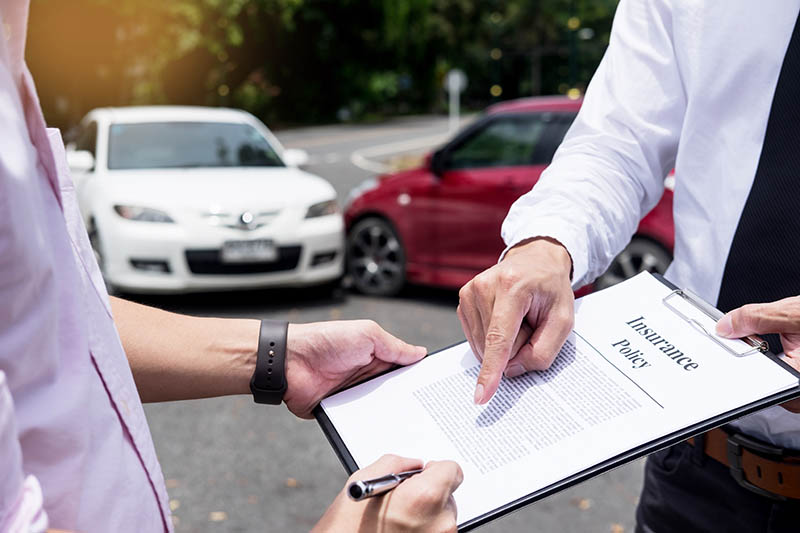 Insurance agent writing on clipboard while examining car after accident claim being assessed and processed