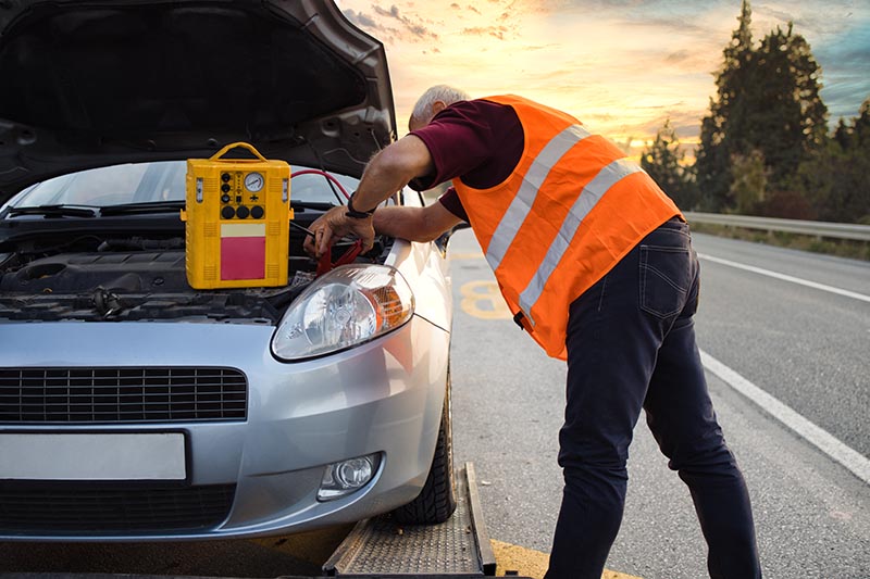 Road assistant worker in towing service trying to start car engine with jump starter
