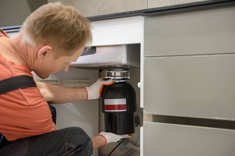 The worker is installing a household waste shredder for the kitchen sink