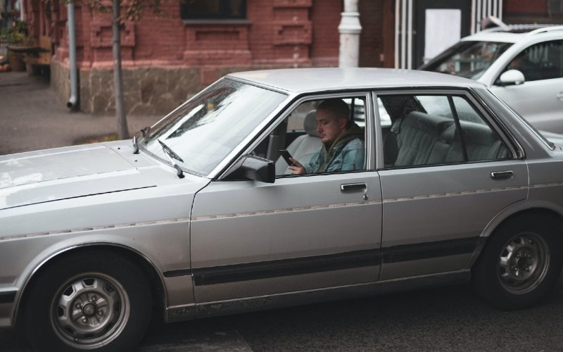 a young person using their phone inside their silver sedan car