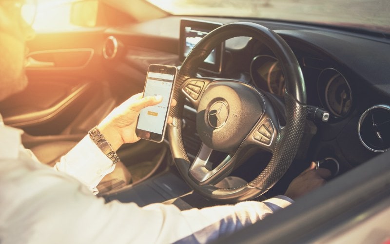 man using their phone as they start their car