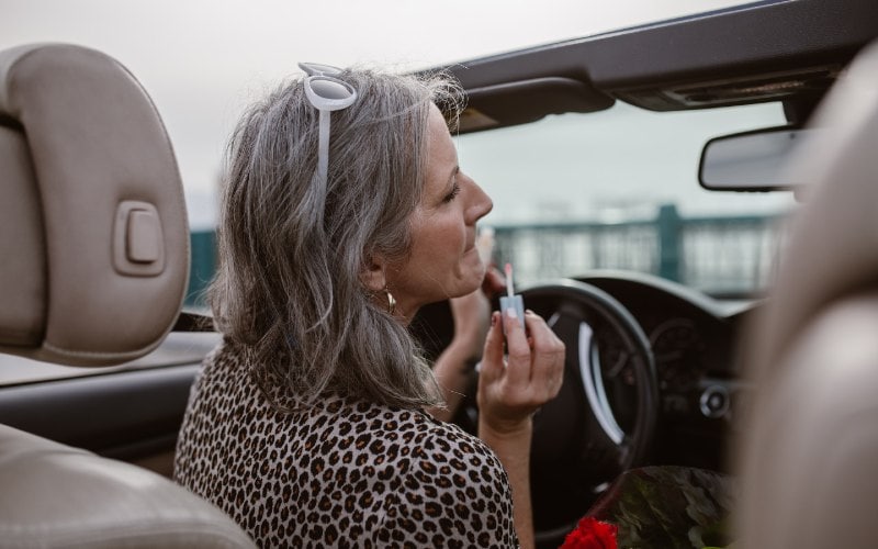 woman applying lip gloss makeup while driving a car