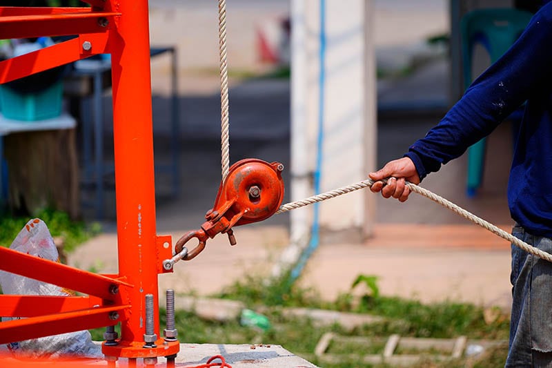 Worker pulling rope by fixed pulley at construction site