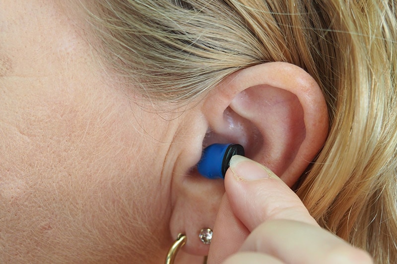 woman putting ear plug into her ear