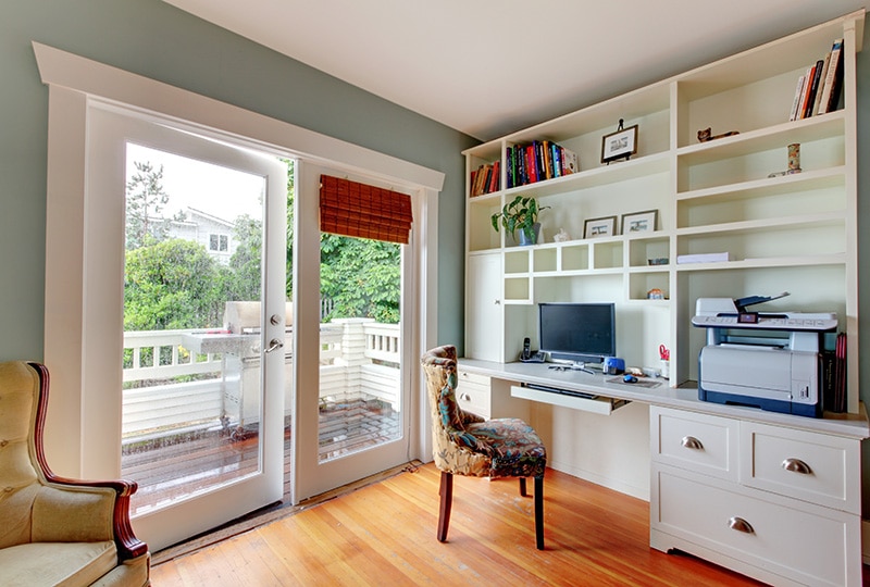 Home office with white open shelves, hardwood floor and blue walls