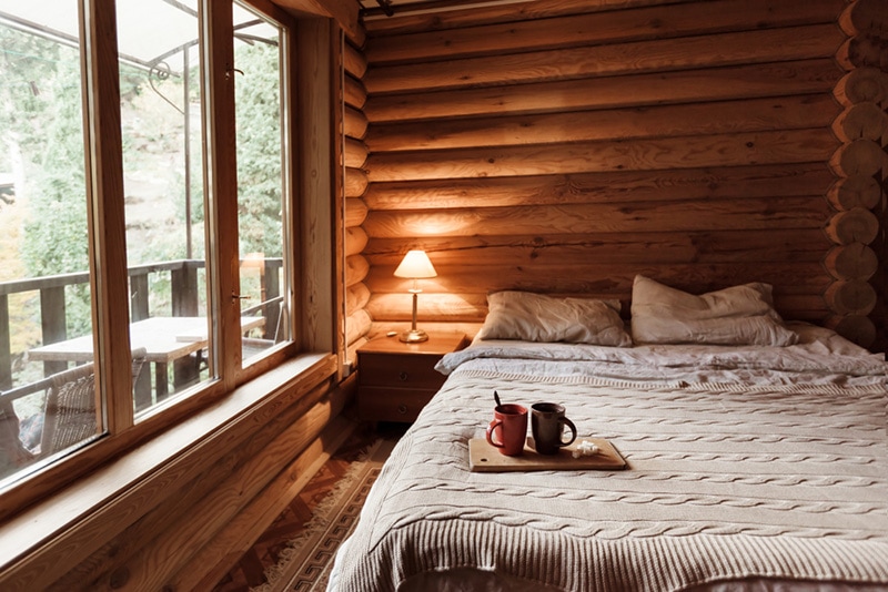 Rustic interior of log cabin bedroom. Cozy bed by big window