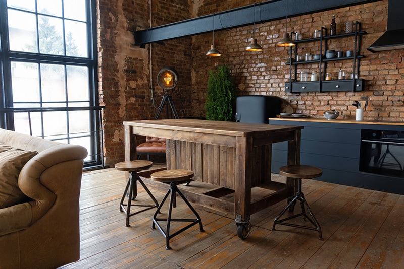 Side view on a wooden table and spacious industrial loft kitchen with vintage decor and black cabinets