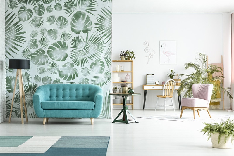 Spacious room with lamp next to blue couch against green wallpaper and pink chair near workspace
