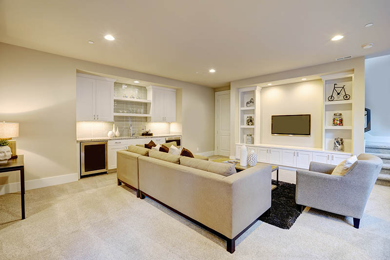 Chic basement features a gray sectional facing a white built-in tv cabinet and wet bar mounted to a wall