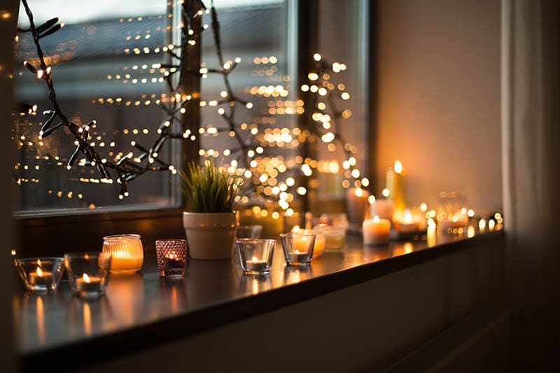 candles burning in lanterns on window sill and festive garland string at home